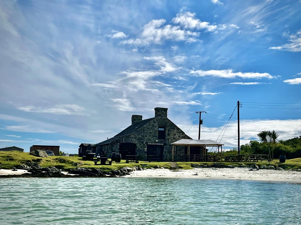 The Boathouse restaurant from the sea with white sandy beach in front of it and a blue sky.