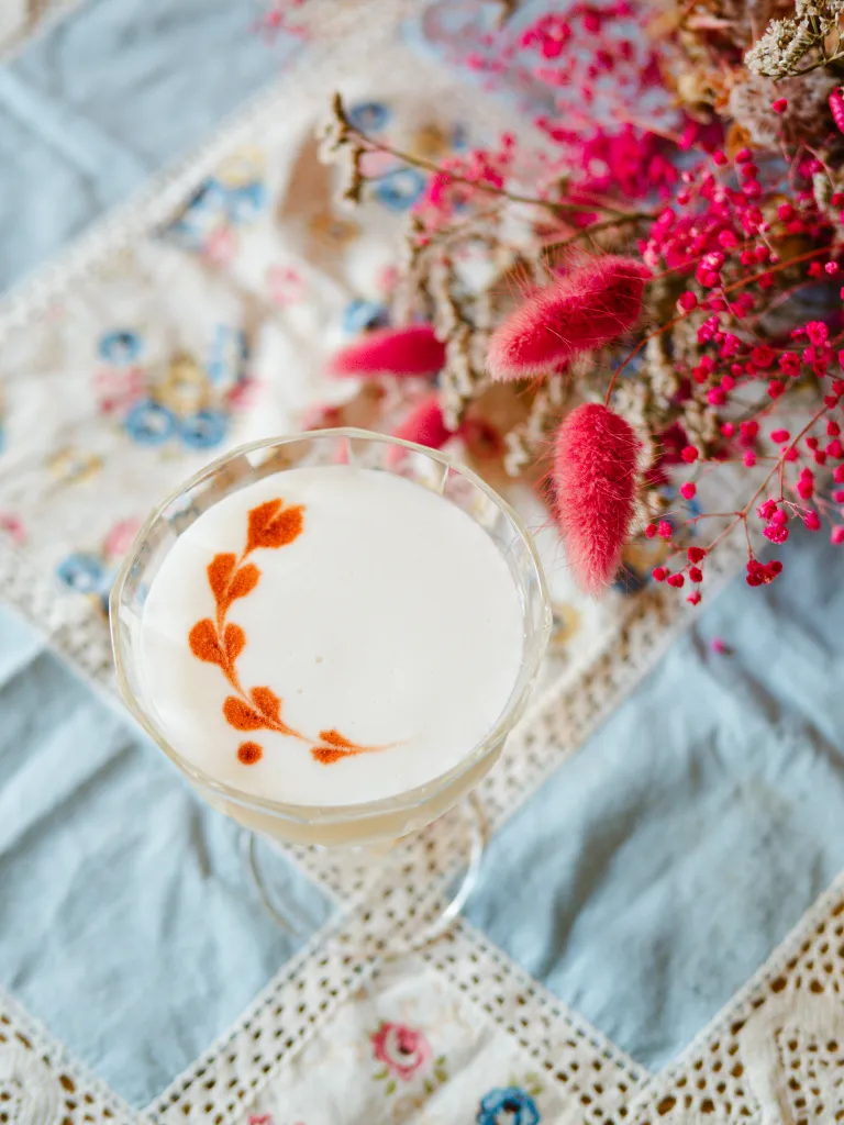 Sour cocktail with bitters used for decorating the foam. Dried pink flowers next to the cocktail