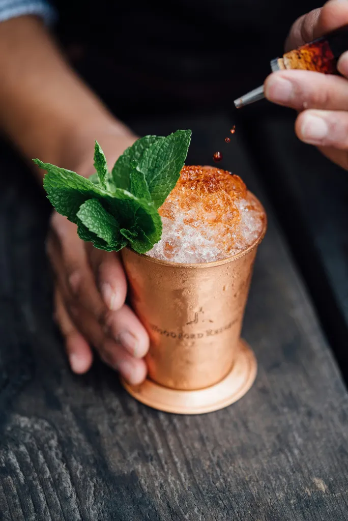 cocktail bitters being added into a mint julep cocktail served in a copper tumbler.